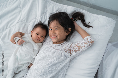 Photography asian daughter kid with infant sibling playing on bed wearing white together