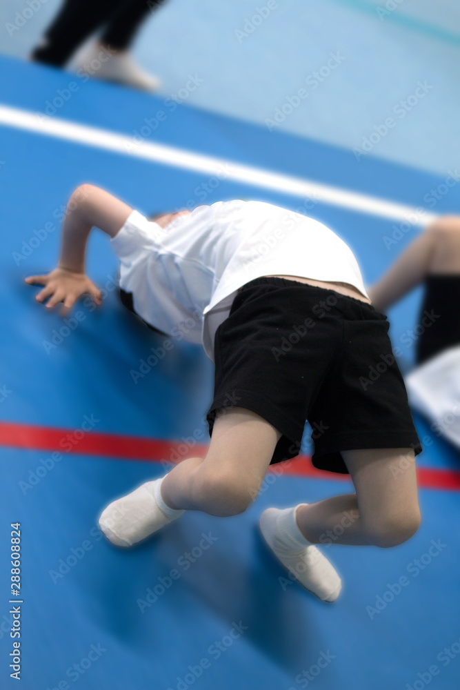 The boy is engaged in acrobatics. A child dressed in a white t-shirt is doing exercises. The boy is engaged in acrobatics. A child dressed in a white t-shirt is doing exercises.