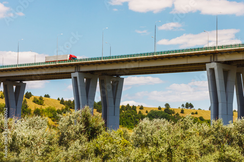 The modern bridge above a green forest and a truck on it with blue sky background. Highway M4 "Don", Rossosh river, Rostov-on-Don region, Russia © Alexey Slyusarenko
