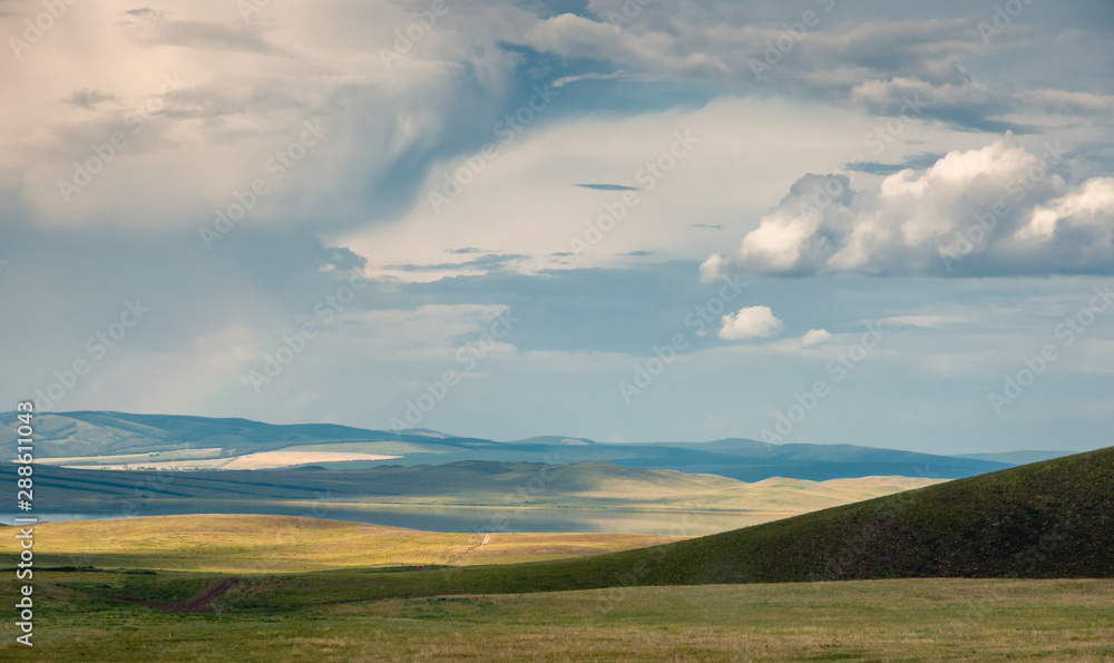 Panoramic landscape with steppe covered with green and yellow grass under blue sky with heavy clouds at Khakassia, Siberia, Russia. Panoramic landscape with steppe covered with green and yellow grass under blue sky with heavy clouds at Khakassia, Siberia, Russia.
