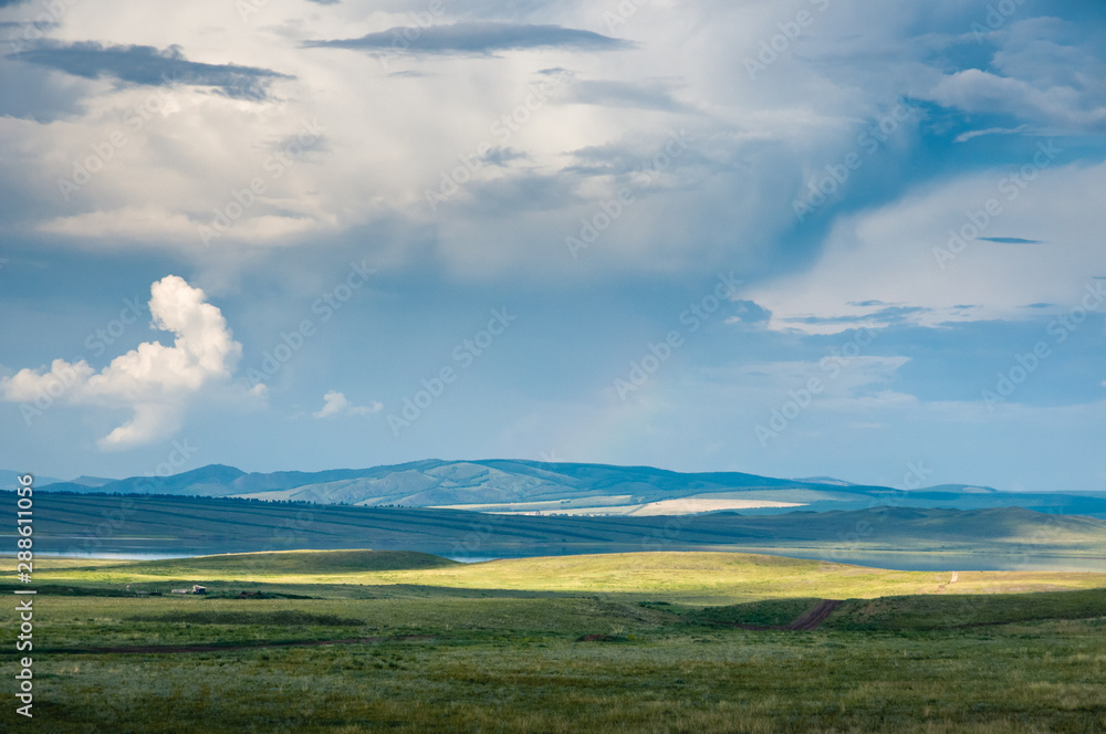 Panoramic landscape with steppe covered with green and yellow grass under blue sky with heavy clouds at Khakassia, Siberia, Russia. Panoramic landscape with steppe covered with green and yellow grass under blue sky with heavy clouds at Khakassia, Siberia, Russia.