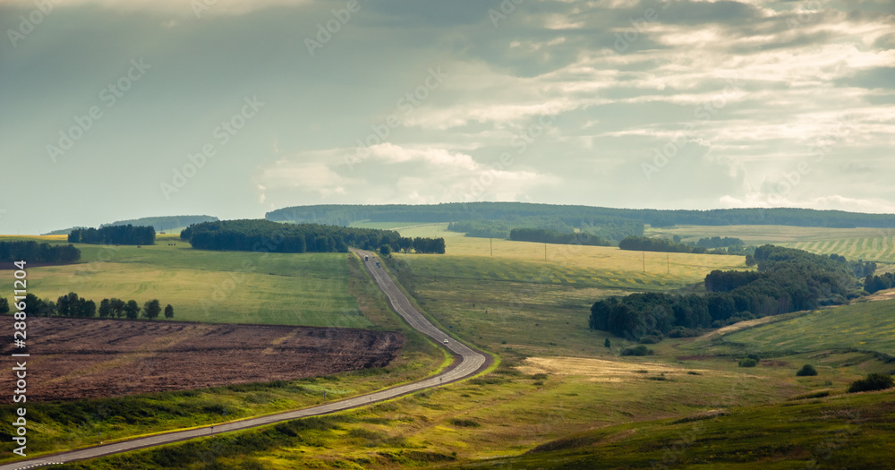 Sunset landscape with agricultural fields in steppe with forest and curvy asphalt road to the horizon at Khakassia, Siberia, Russia.