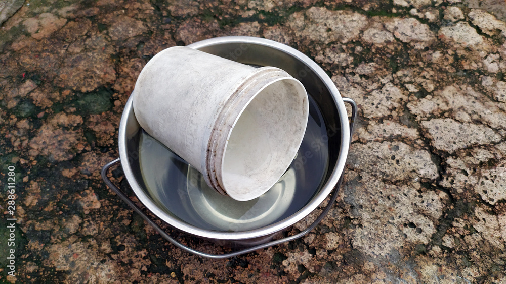 a steel bucket fill with water and plastic mug in this a steel bucket fill with water and plastic mug in this