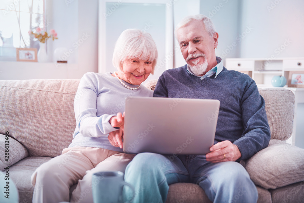 Modern retired couple feeling involved in watching film on their laptop