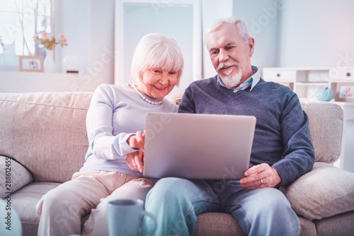 Modern retired couple feeling involved in watching film on their laptop