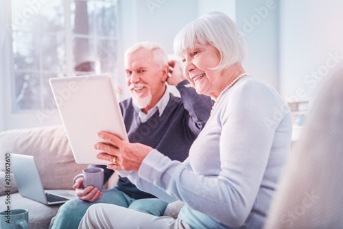 Beaming grandparents using devices watching photos of their children