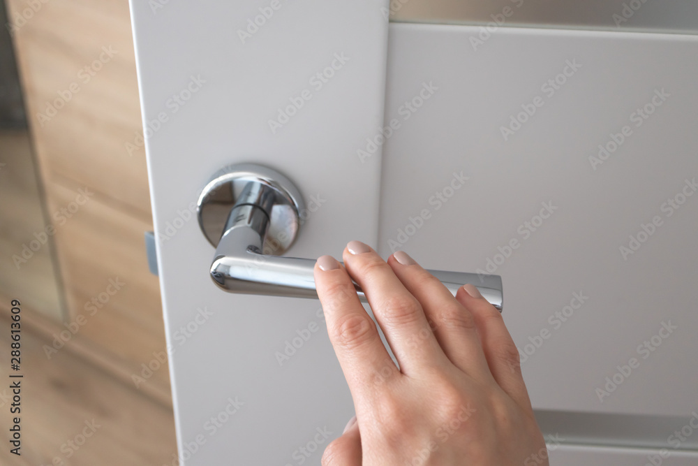 Female hand on metal door handle. Modern interior detail - obrazy, fototapety, plakaty 
