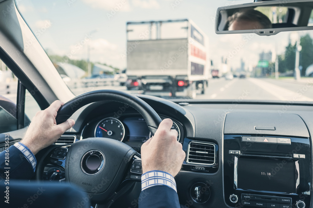 Selective focus of hands of businessman on steering wheel, driving a car on the highway.