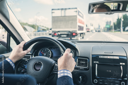 Selective focus of hands of businessman on steering wheel, driving a car on the highway.