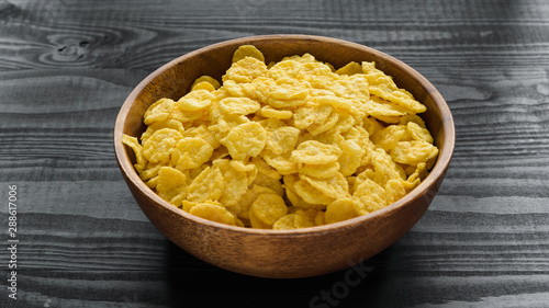 wooden bowl with cornflakes on a dark wooden background