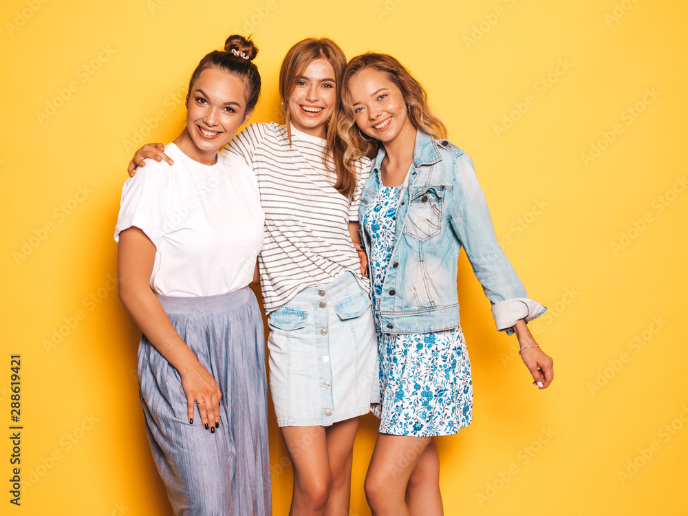 Three young beautiful smiling hipster girls in trendy summer clothes. Sexy carefree women posing near yellow wall in studio. Positive models going crazy and having fun Three young beautiful smiling hipster girls in trendy summer clothes. Sexy carefree women posing near yellow wall in studio. Positive models going crazy and having fun