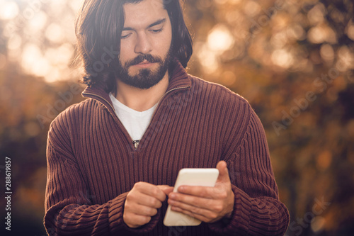 Modern man using cellphone in the autumn colored park. photo