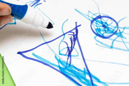 A closeup view of a child drawing colorful pictures with a blue felt tip marker pen on white paper  preschool art and education  learning and development of infants.