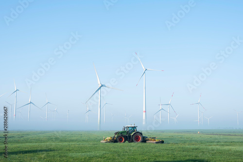 Photography farmer mows grass near wind turbine farm in oastfriesland on misty summer mornin