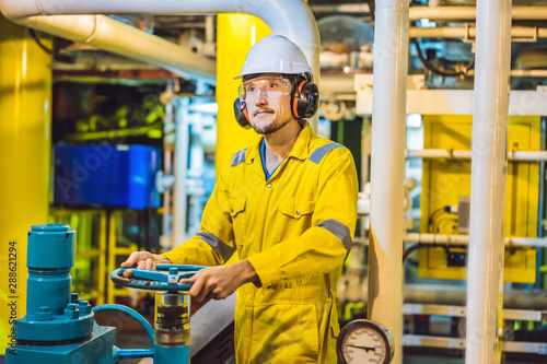 Young man in a yellow work uniform, glasses and helmet in industrial environment,oil Platform or liquefied gas plant photo