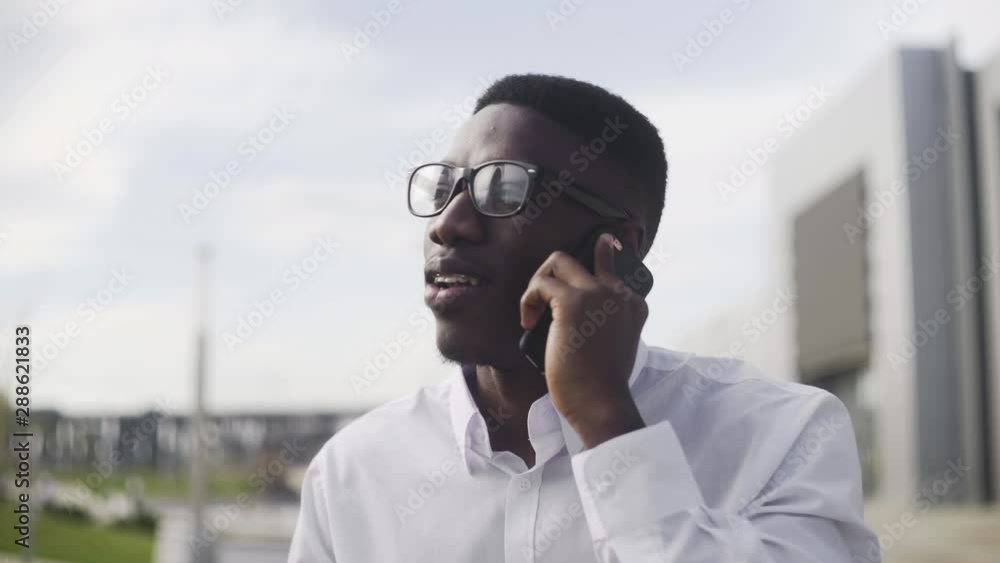 Young African Businessman with braces talking on cell phone in city park Young African Businessman with braces talking on cell phone in city park