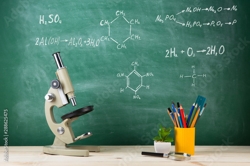 Education concept - microscope on the desk in the auditorium, blackboard background