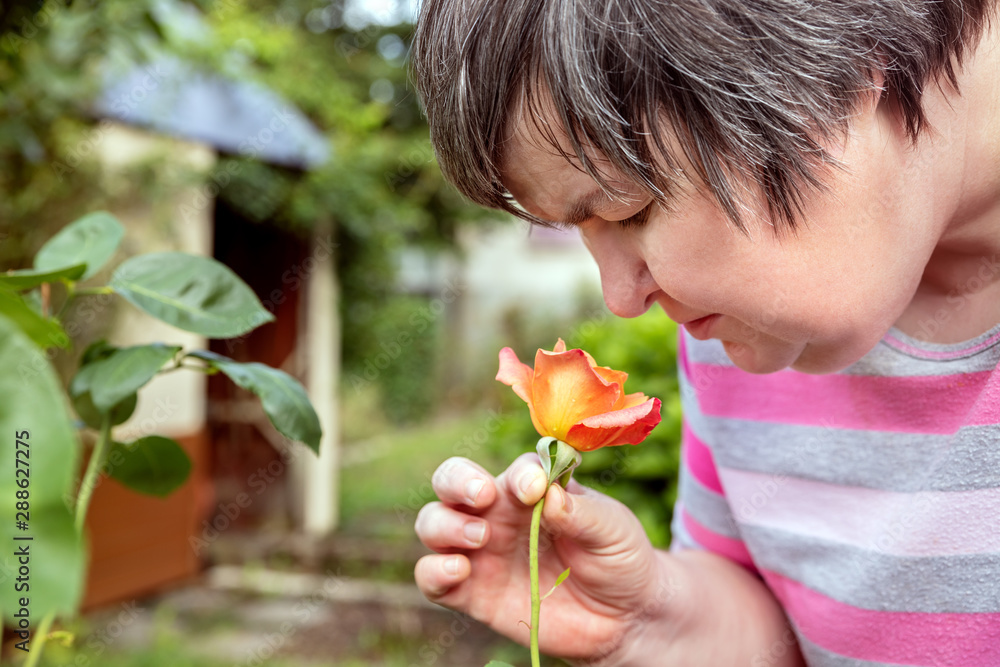Frau mit geistiger Behinderung riecht an einer Rose im Garten, Bewusstsein und Selbstbestimmung Frau mit geistiger Behinderung riecht an einer Rose im Garten, Bewusstsein und Selbstbestimmung