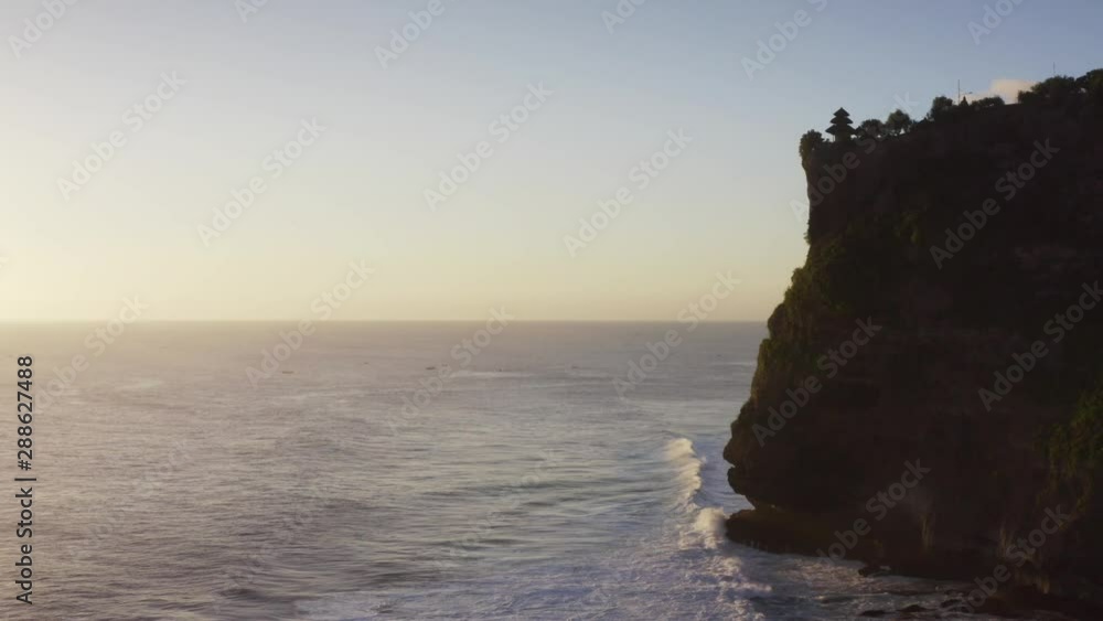 Aerial view of picturesque breathtaking cliffs above the ocean. Silhouette of holy Pura Uluwatu temple on the cliff top. Twilight, evening. Bali, Indonesia Aerial view of picturesque breathtaking cliffs above the ocean. Silhouette of holy Pura Uluwatu temple on the cliff top. Twilight, evening. Bali, Indonesia