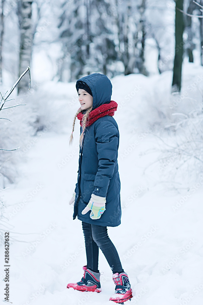 child  playing in the snow / the girl in warm sports clothes is playing with snow on a winter walk. Warm woolen hat, down jacket. Concept of a happy baby walk.