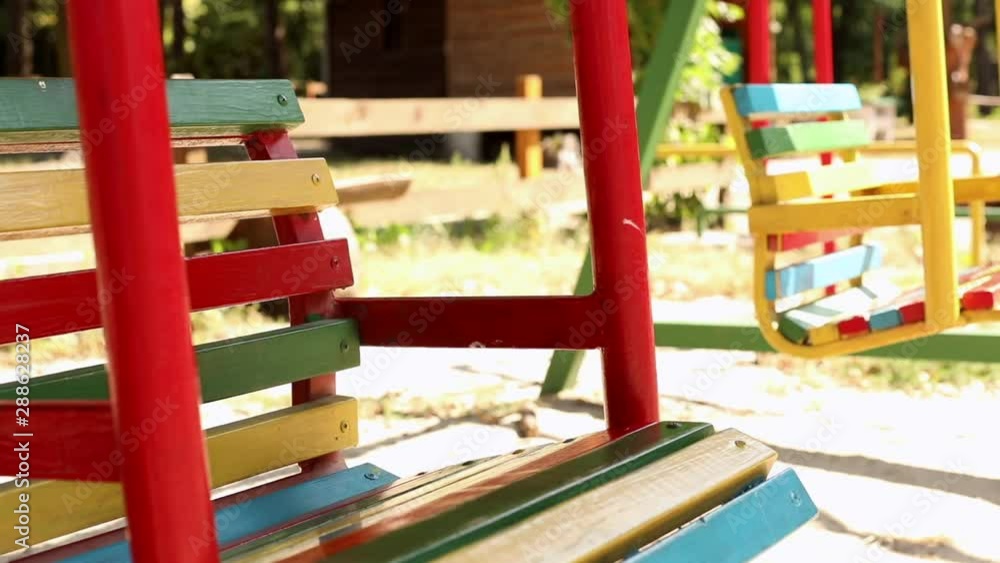 Close-up view of empty colorful bright swings at child playground loop outside with summer sunshine on background. Happy childhood, family concept. Close-up view of empty colorful bright swings at child playground loop outside with summer sunshine on background. Happy childhood, family concept.