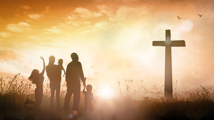 Silhouette of family with children looking at christian cross at sunrise for hope, faith and spiritual concept