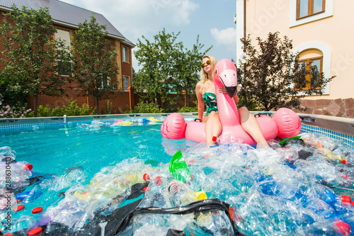 Problem of trash, plastic recycling, pollution and environmental concept - silly woman swims and have fun in a polluted pool. Bottles and plastic bags float near her