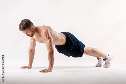young man with a beard of a sports physique doing push-ups from the floor on a white isolated background, sportsman goes in for sports