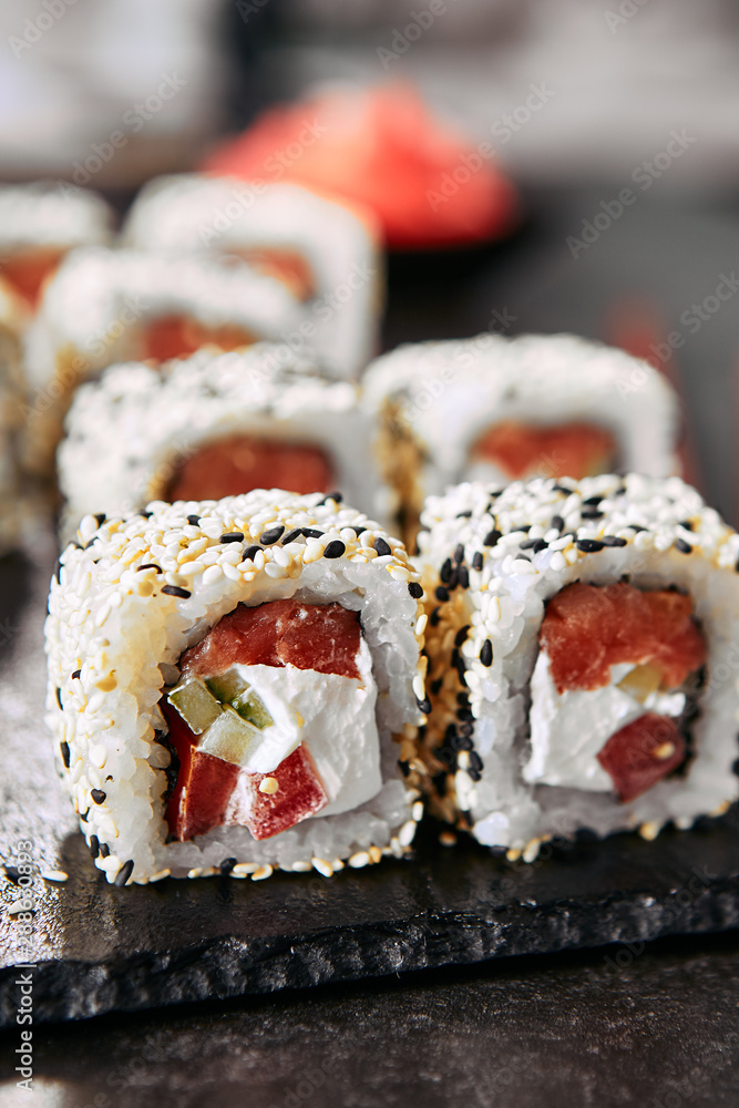 Tokyo salmon uramaki sushi with rice, cream cheese, tomatoes, cucumber, sesame and nori close up. Macro shot of japanese food uramaki rolls with smoked fish and fresh vegetables Tokyo salmon uramaki sushi with rice, cream cheese, tomatoes, cucumber, sesame and nori close up. Macro shot of japanese food uramaki rolls with smoked fish and fresh vegetables