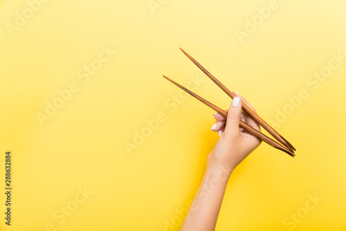 Female hand with chopsticks on yellow background. Traditional asian food with emty space for your design photo