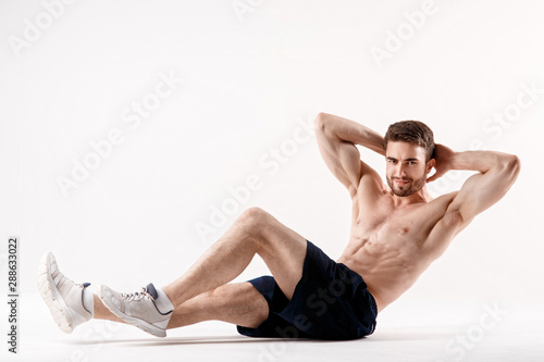 young man with a beard of a sports physique does an exercise on the muscles of the abdominal cavity on a white isolated background, the athlete goes in for sports, exercise on the muscles of the press