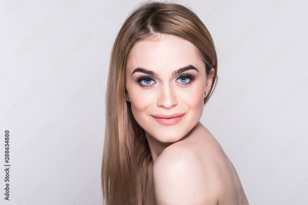 Beautiful healthy blond woman is posing with naked shoulders. She is standing and smiling. The lady is looking at camera happily and touching face. Beautiful healthy blond woman is posing with naked shoulders. She is standing and smiling. The lady is looking at camera happily and touching face.