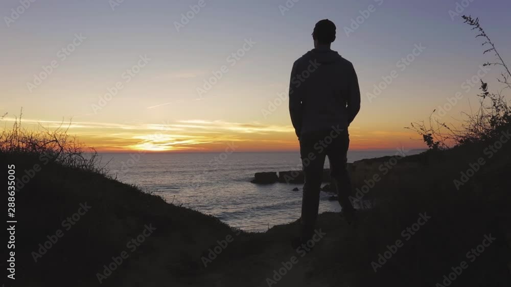 Young man looking at sunset by the coastline on top of a cliff. Young man looking at sunset by the coastline on top of a cliff.