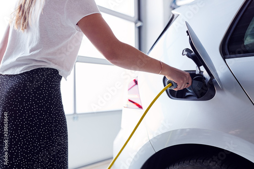Canvas Print Close Up Of Woman Charging Electric Vehicle With Cable In Garage At Home