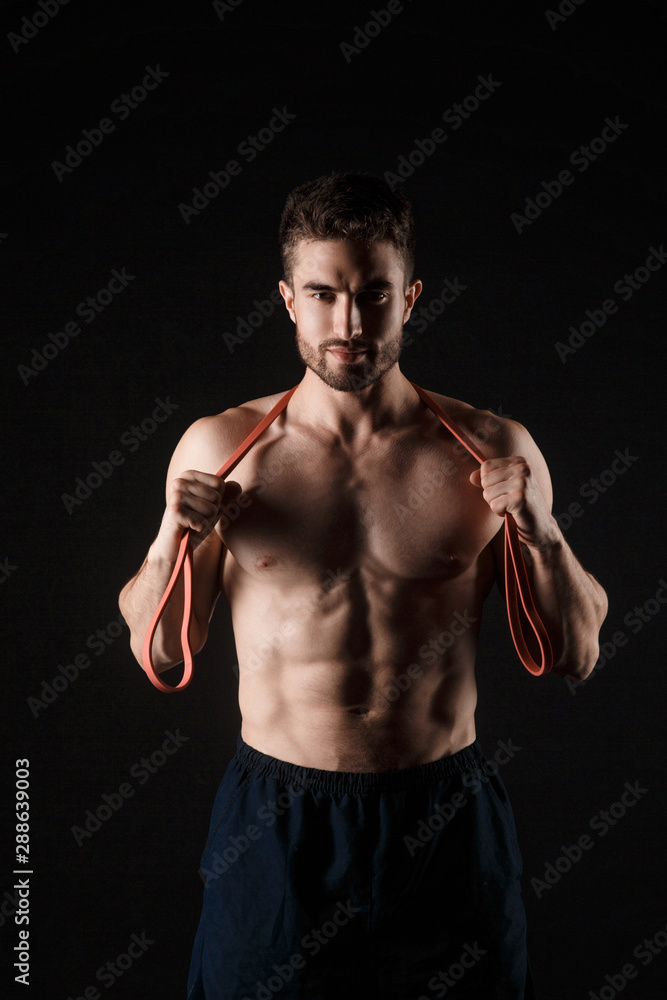 sports man with a beard on a black background with gymnastic elastic bands in hands