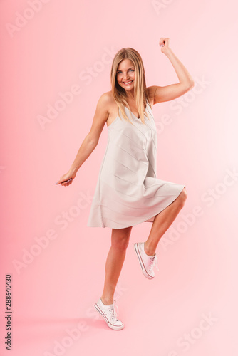 Full length image of young blond woman wearing dress smiling and dancing