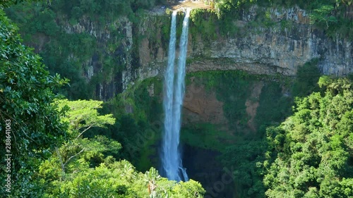 A shot of a double jet waterfall falling over a natural rock wall, in a very leafy place. photo