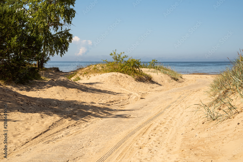 Road with tire marks sprinkled with sand going to the sea through the dunes Road with tire marks sprinkled with sand going to the sea through the dunes
