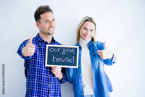 Young beautiful couple holding blackboard standing over isolated white background happy with big smile doing ok sign, thumb up with fingers, excellent sign