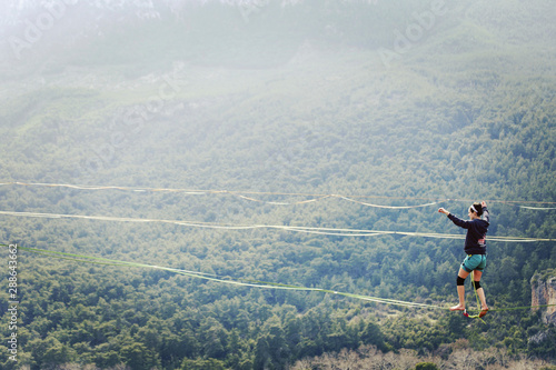 A woman is walking along a stretched sling. Highline in the mountains. Woman catches balance. Performance of a tightrope walker in nature. Highliner on the background of valley.