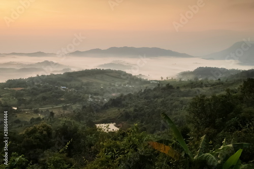Mountain view misty morning of top hills and green forest around with sea of fog with yellow sun light in the sky background, sunrise at ITTI View Point, Khao Kho, Phetchabun, Thailand.