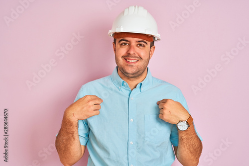 Young architect man wearing security helmet standing over isolated pink background looking confident with smile on face  pointing oneself with fingers proud and happy.