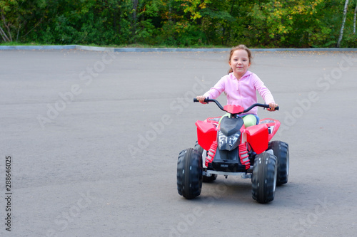 Little girl is riding on a electric quadricycle. Children's summer vacation and entertainments.
