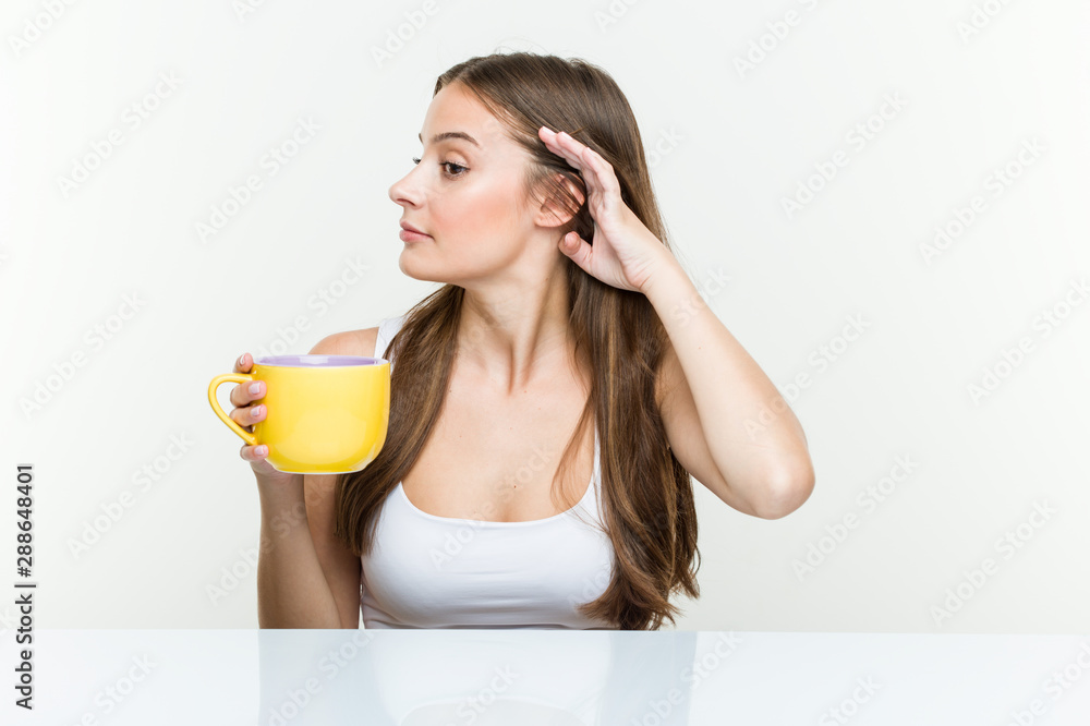 Young caucasian woman holding a cup trying to listening a gossip. Young caucasian woman holding a cup trying to listening a gossip.