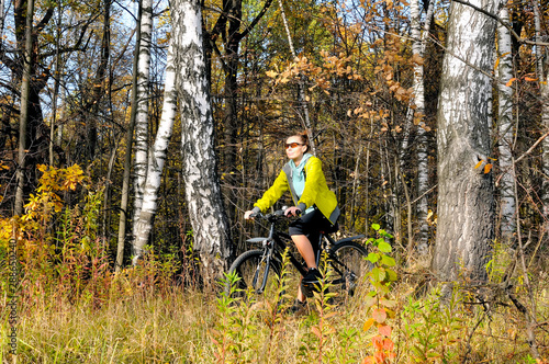 Young slim girl on a bicycle in autumn birch forest