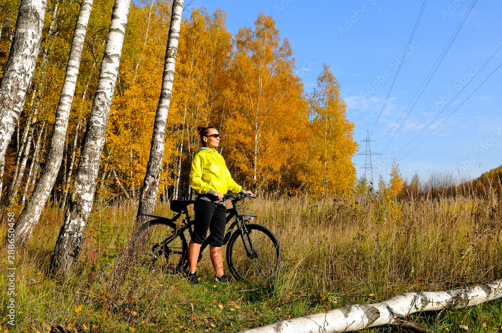 Obraz premium Young slim girl on a bicycle in autumn birch forest