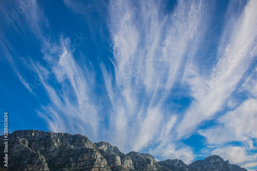 Fototapeta Naklejka Na Ścianę i Meble -  Dramatic blue sky with streaks of vertical clouds over mountain range.