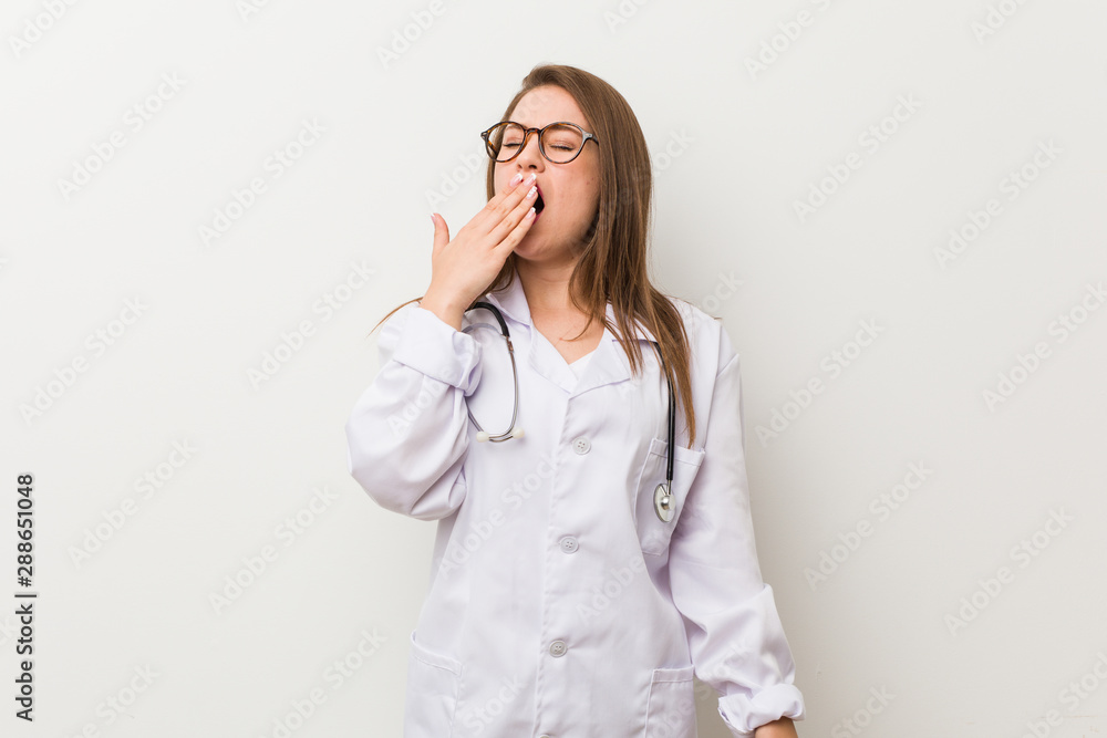 Young doctor woman against a white wall yawning showing a tired gesture covering mouth with hand. Young doctor woman against a white wall yawning showing a tired gesture covering mouth with hand.