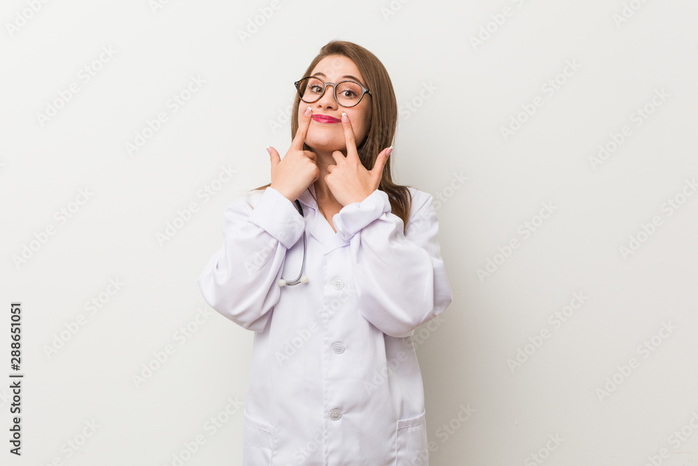 Young doctor woman against a white wall doubting between two options. Young doctor woman against a white wall doubting between two options.