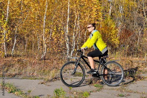Girl on bicycle on a path in the autumn forest